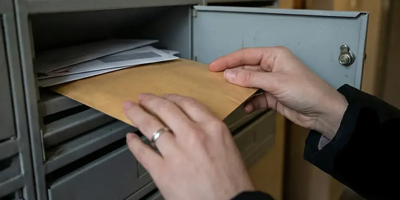 Ręce wyjmują kopertę z brązowego papieru ze skrzynki pocztowej, co może symbolizować nieodebranie nakazu zapłaty przez pozwanego.