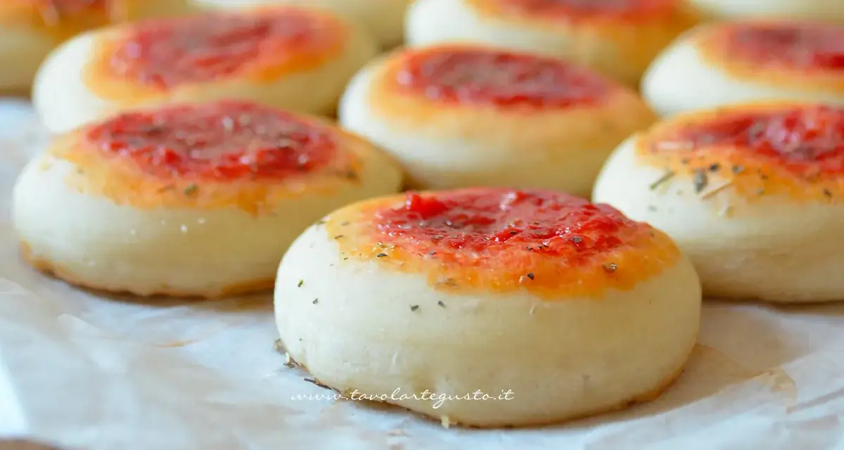 Pizzette fatte in casa, piccole e invitanti, con un soffice impasto e un tocco di pomodoro e erbe aromatiche.