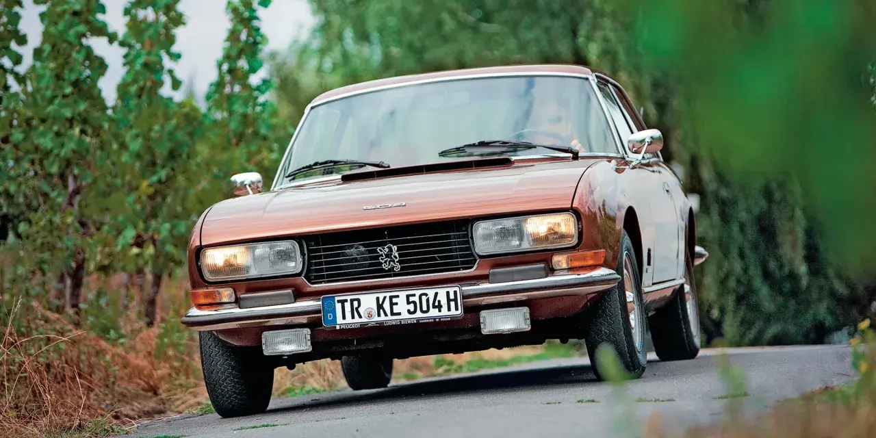 Klasyczny brązowy Peugeot 504 Coupe jedzie po krętej drodze wśród zieleni.