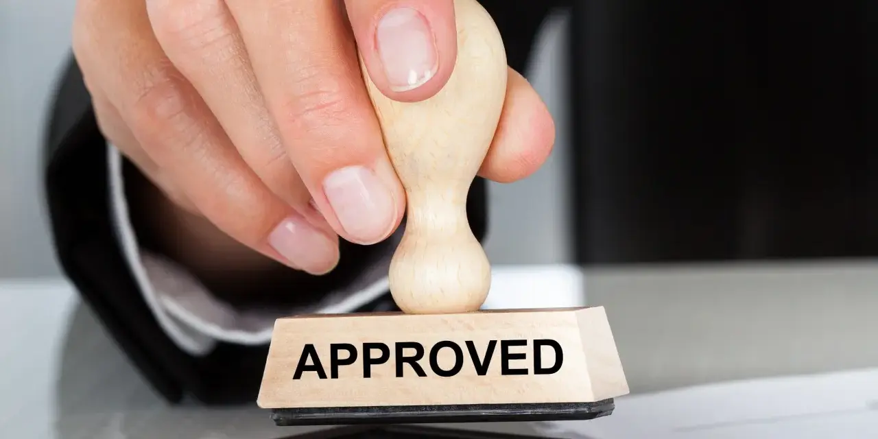 Dłoń z pieczątką "APPROVED" nad poduszką z tuszem. To symbol zatwierdzenia, jak certyfikat AEO.