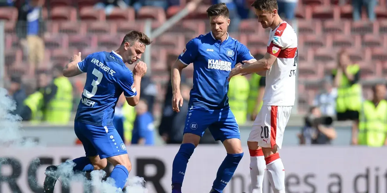 Piłkarze Karlsruher SC w niebieskich strojach, jeden z nich z numerem 3, otoczeni dymem z rac.