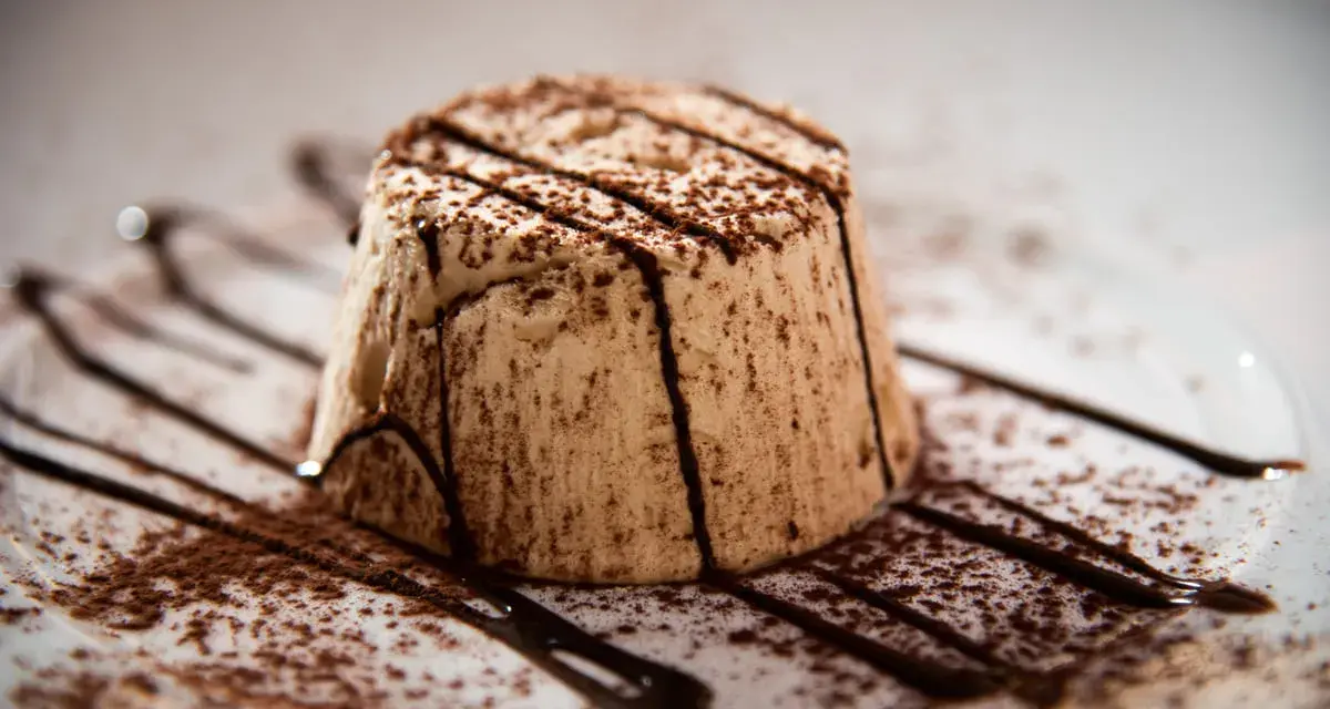 Delizioso parfait di mandorle, spolverato di cacao e decorato con scaglie di cioccolato fondente su un piatto bianco.