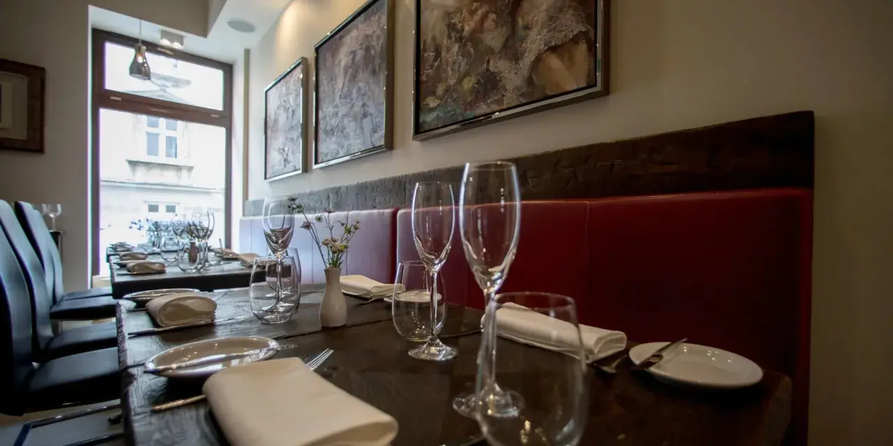 Elegancko nakryte stoły w restauracji z gwiazdką Michelin w Polsce. Czerwone obicia, obrazy na ścianach i kieliszki zapraszają na wyjątkowe doznania kulinarne.