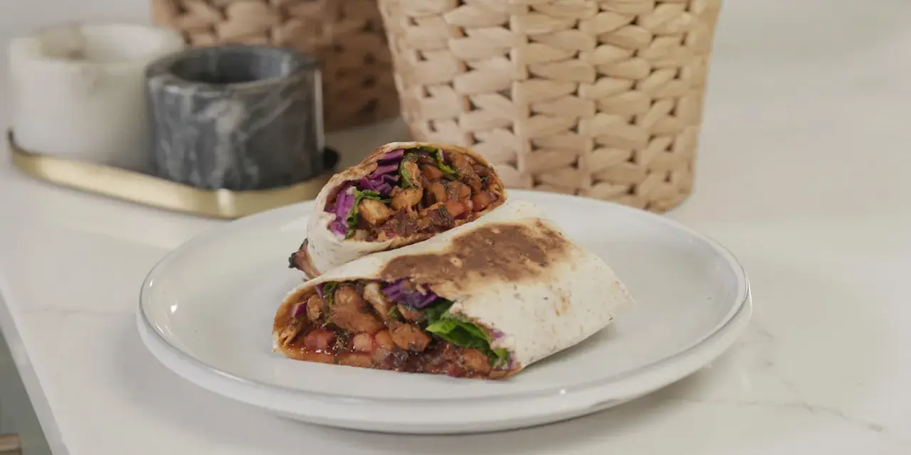 Kebab zawinięty w tortillę, przekrojony na pół, z widocznym nadzieniem z mięsa, warzyw i sosu.