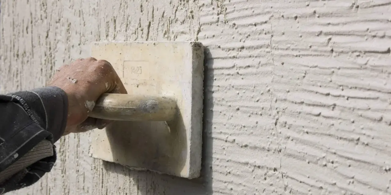 Main d'un artisan appliquant un enduit projeté texturé. Le prix au m2 de ce type de finition est souvent demandé.