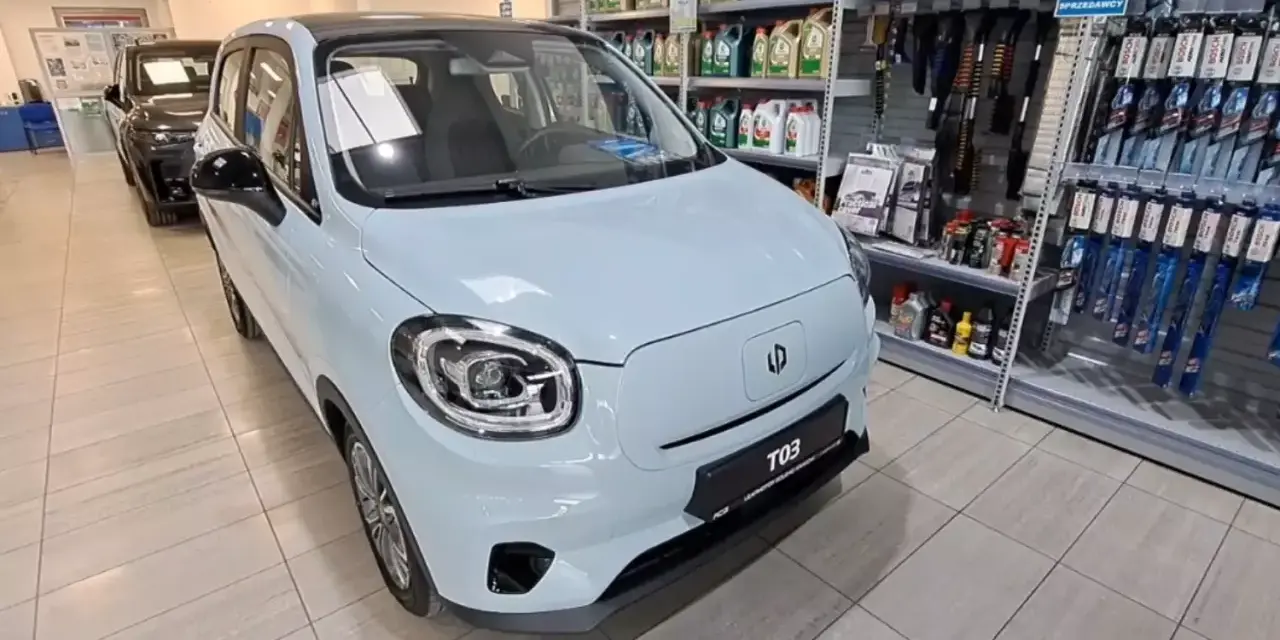 Jasnoniebieski Leapmotor T03 stoi w salonie samochodowym obok półek z akcesoriami.