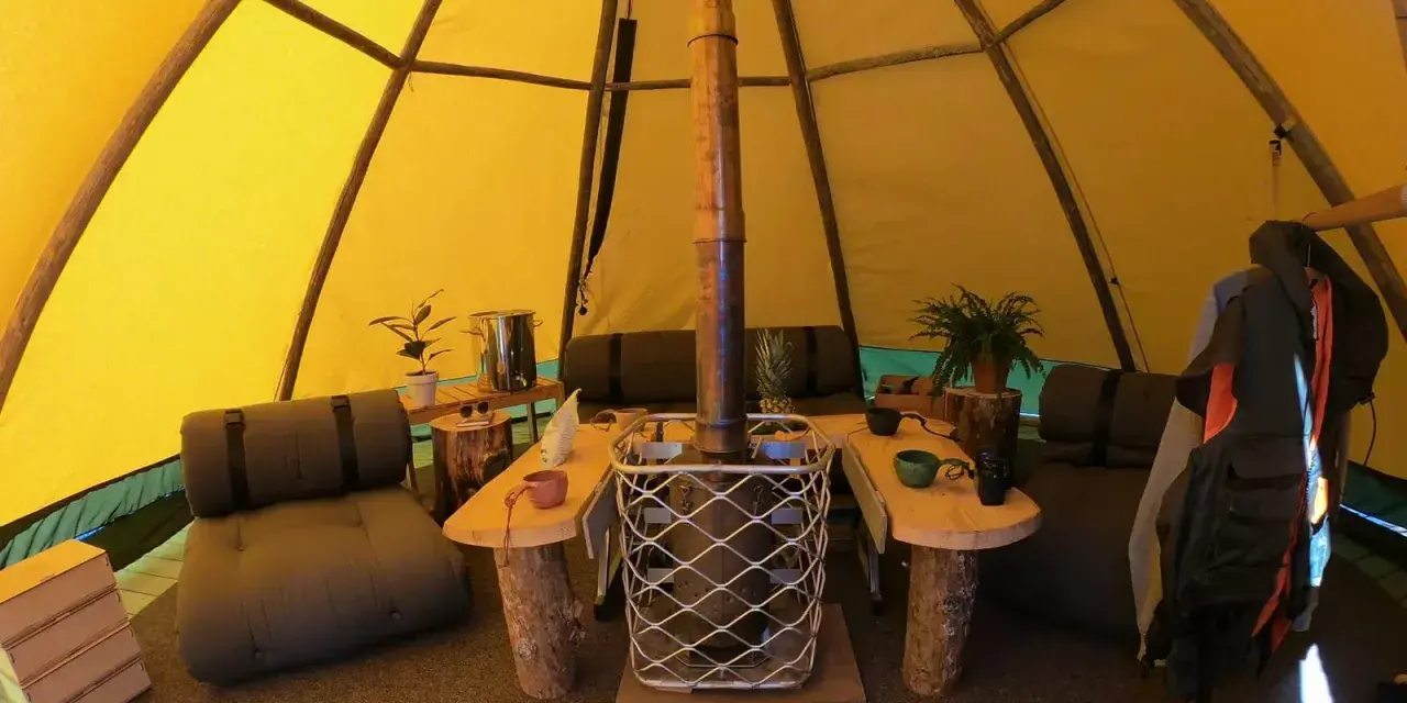 Mysig interiör i ett tipi-tält på Sorsele camping. Här finns sittplatser, ett bord och en kamin för värme.