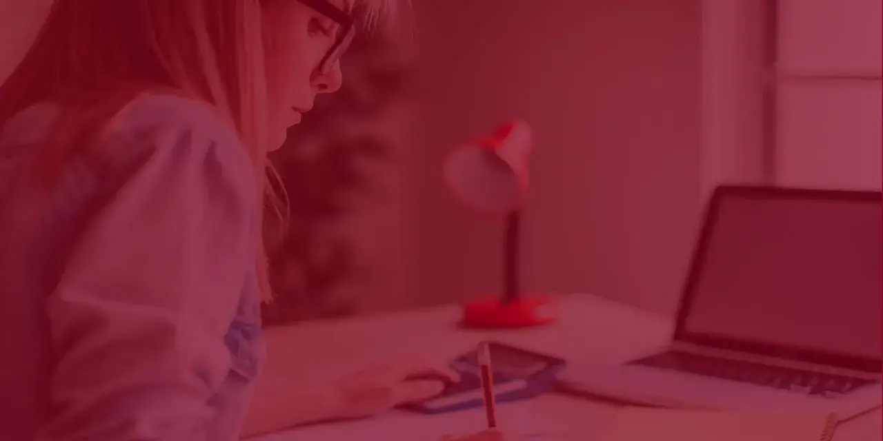 Kobieta z zeszytem i kalkulatorem zastanawia się, ile kosztują studia zaoczne. Obok leży laptop.