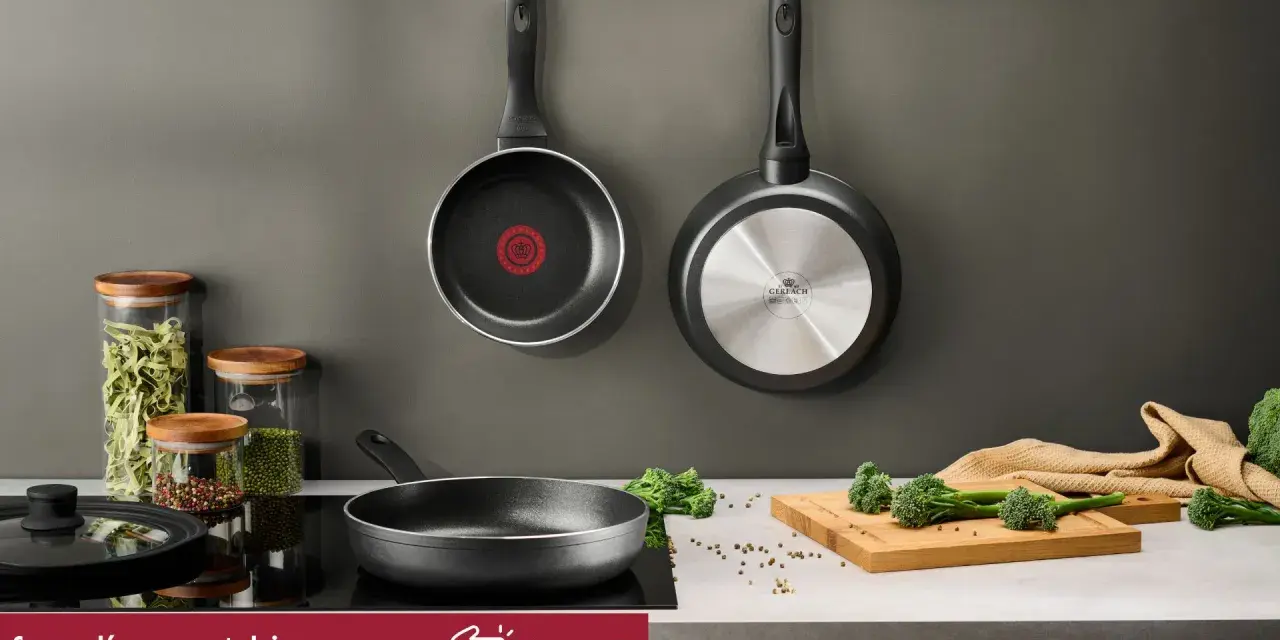 Dwie patelnie wiszące, jedna z logo Tefal, druga Gerlach. Na blacie patelnia, słoiki z makaronem i przyprawami, deska z brokułami. Czy patelnie Tefal można myć w zmywarce? Sprawdź!
