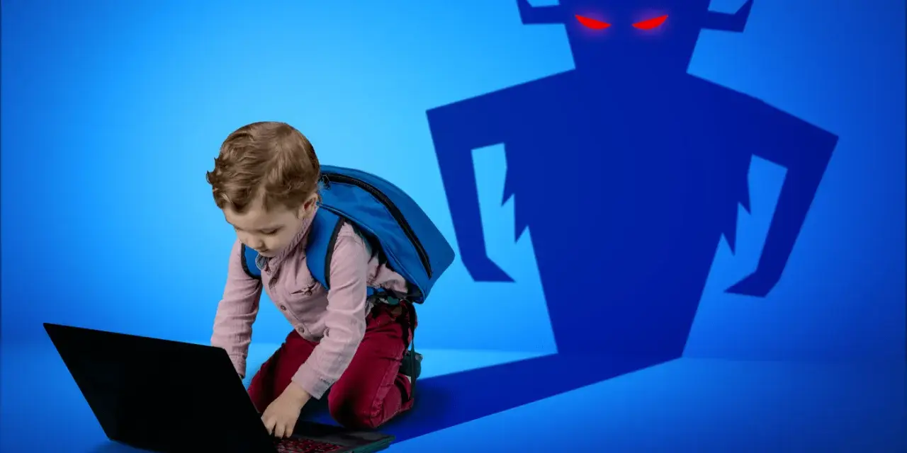 Chłopiec z plecakiem pochyla się nad laptopem, a za nim cień potwora z czerwonymi oczami. Ważne jest zabezpieczenie dziecka w sieci.