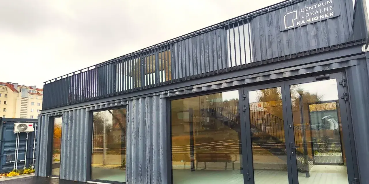 Nowoczesne centrum lokalne Kamionek, zbudowane z kontenerów. Ten innowacyjny kamionkowy materiał budowlany tworzy przestrzeń z przeszklonymi fasadami i balkonem.