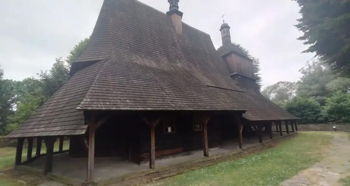 Drewniany kościół w Sękowej z charakterystycznym, wielospadowym dachem krytym gontem, otoczony zielenią.