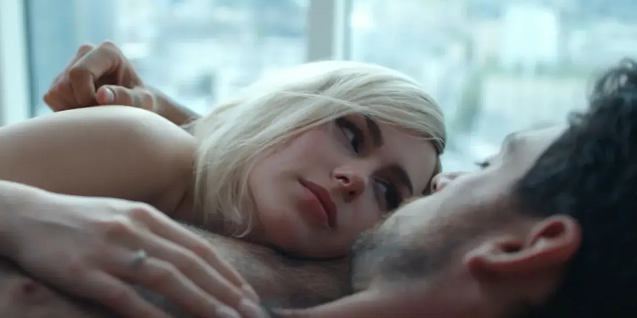 Blondynka i brunet leżą blisko siebie, ich ciała stykają się. Intymna scena, która sugeruje seks na scenie.