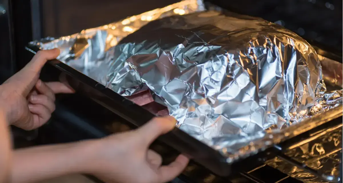 Mains dans un plat recouvert d'aluminium au four, prêt à cuire.