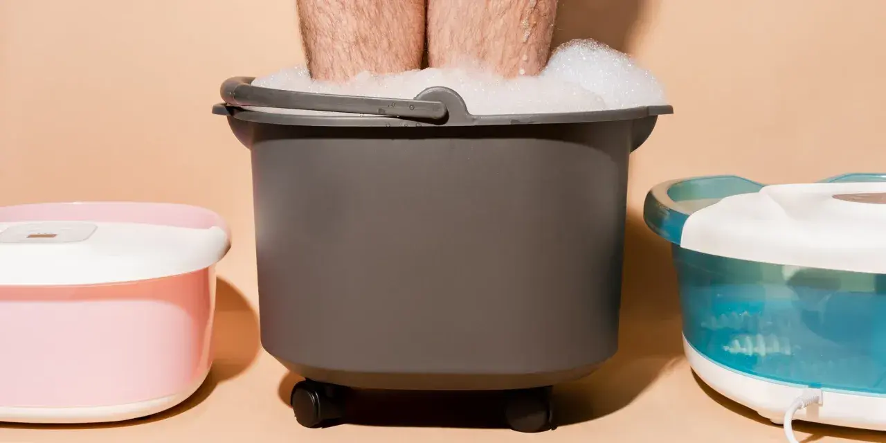 A person's legs are submerged in a foamy foot bath, part of a home foot detox setup with other foot spa machines.