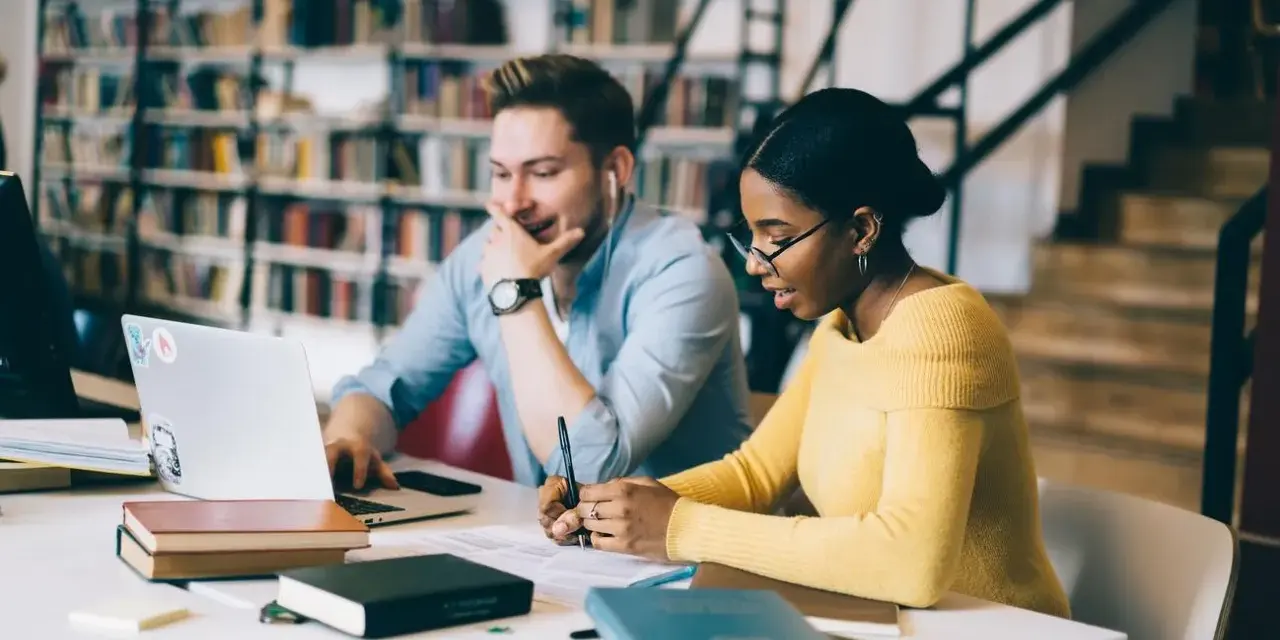 Studenti universitari collaborano a un progetto, immersi in libri e tecnologia.