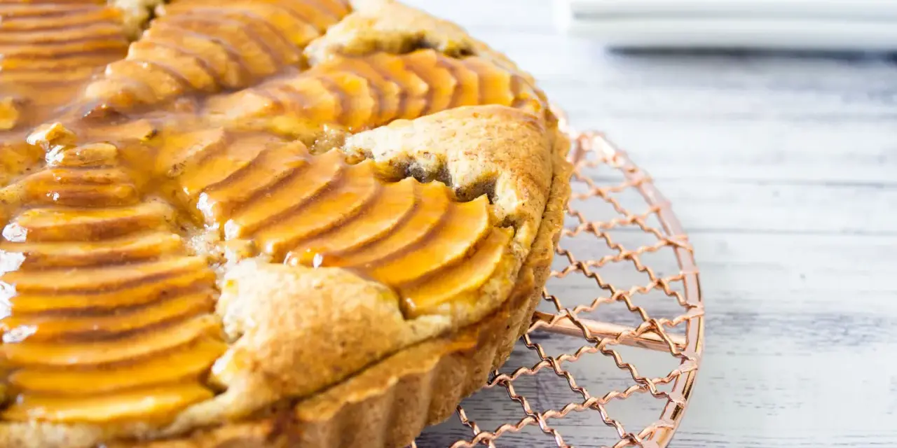 Deliciosa tarta de pera francesa, con peras laminadas y glaseado dorado, enfriándose sobre una rejilla de cobre.