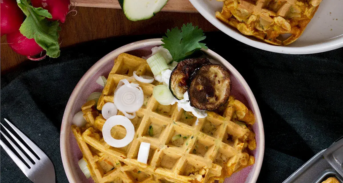 Herzhafte Waffeln mit Zucchini, Zwiebeln und gegrillten Auberginen, garniert mit Kräutern und einem Klecks Joghurt.