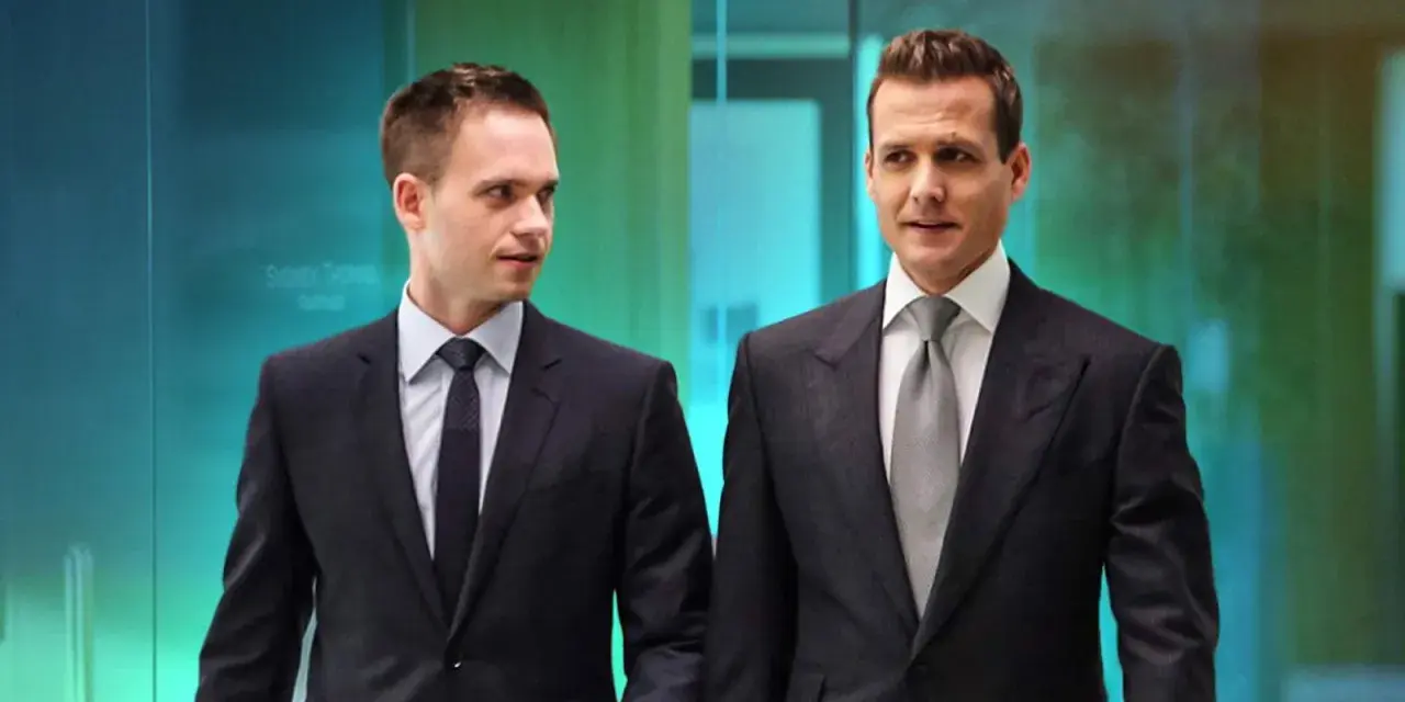Due uomini in abiti eleganti, stile Harvey Specter, camminano in un ufficio moderno.