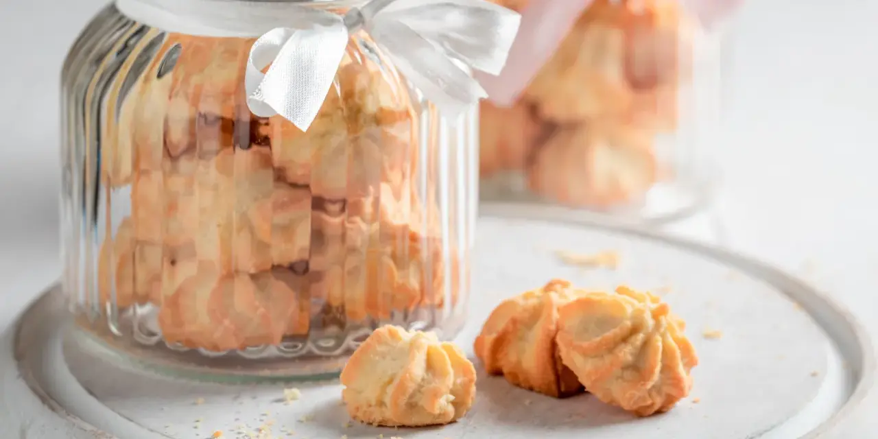 Biscuits sablés dans des bocaux en verre décorés de rubans blancs et roses, parfaits pour un dessert pique-nique.