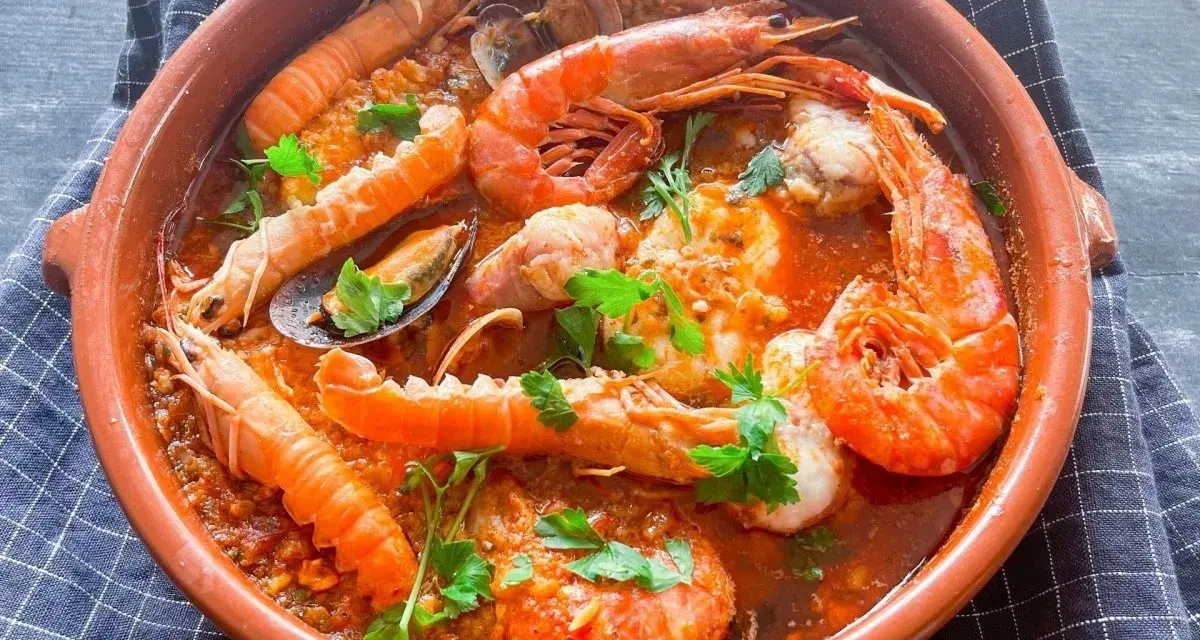 Deliciosa zarzuela de pescado con gambas, mejillones y cigalas en una cazuela de barro, adornada con perejil fresco.