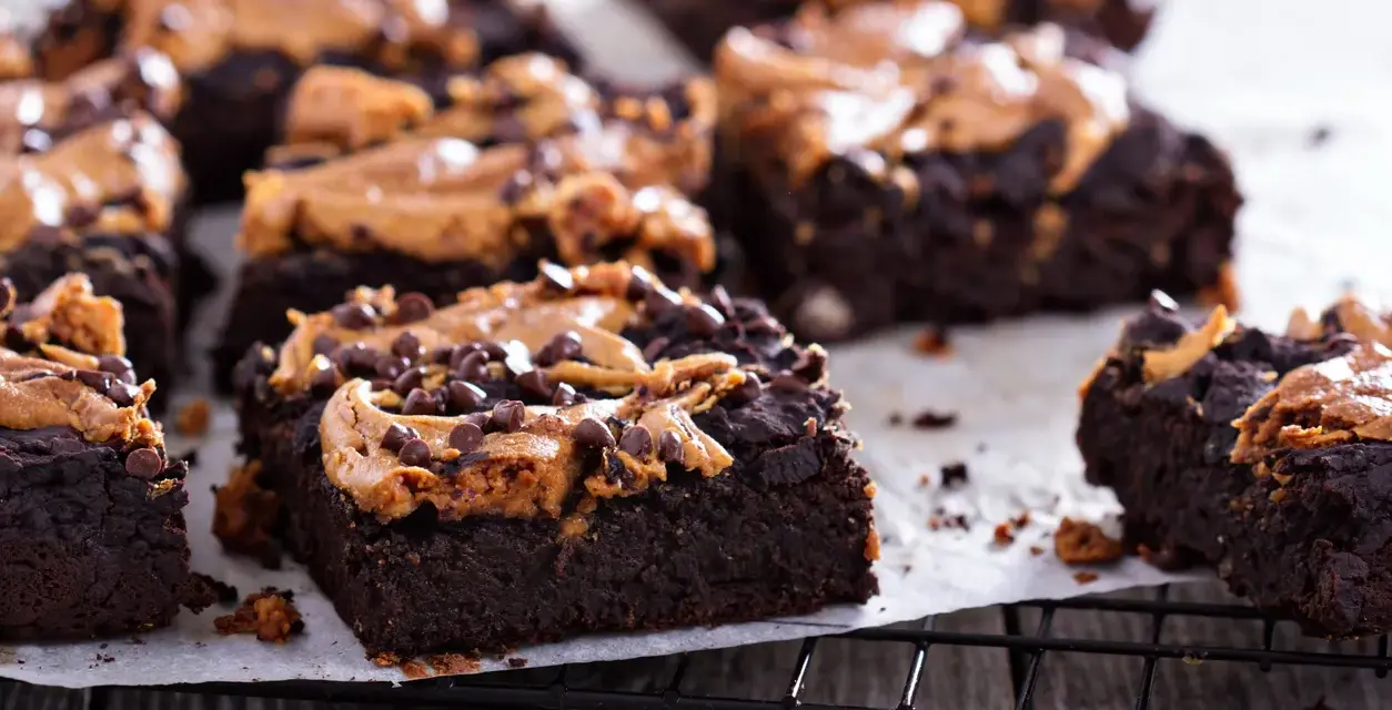 Pyszne brownie z bananami i masłem orzechowym, posypane czekoladowymi kropelkami, kuszą na czarnej kratce.