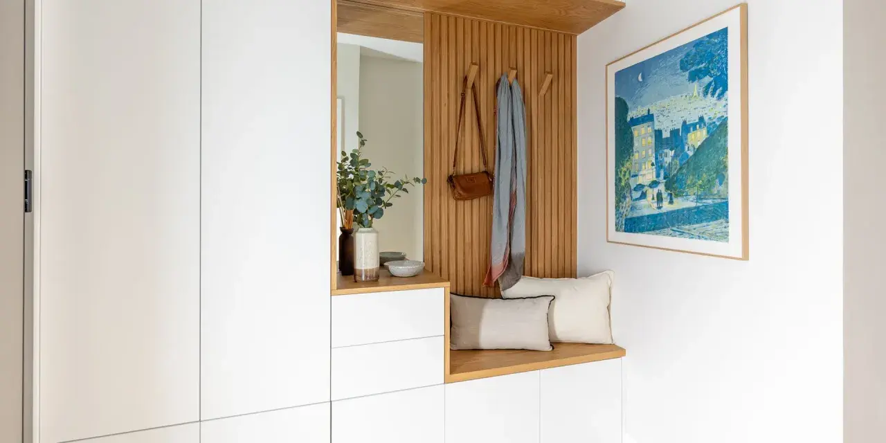 Ideas para decorar recibidor pequeño: banco de madera, espejo, perchero con bolso y bufanda, cuadro y armarios blancos.