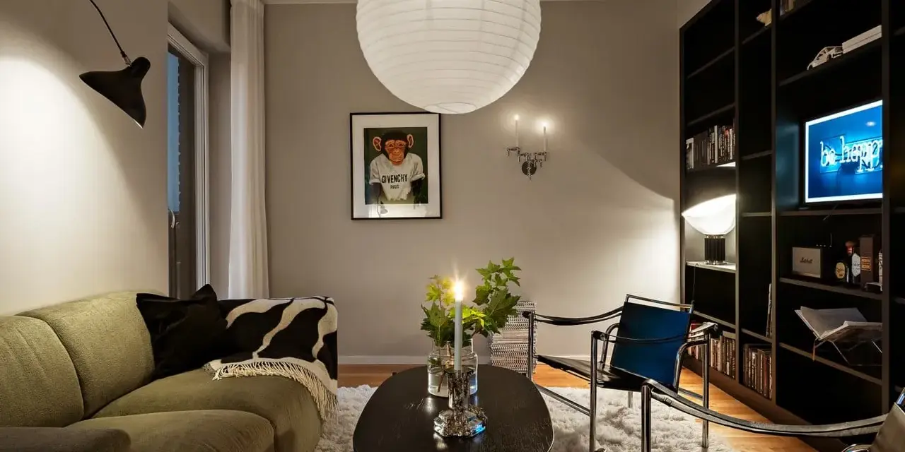 Mysig vardagsrumsmiljö med en stor taklampa, en svart vägglampa och en bokhylla full med böcker. Perfekt lampor inspiration för ditt hem.
