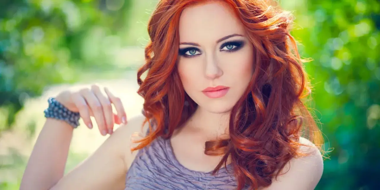 Une femme aux cheveux roux et au maquillage smoky eyes parfait, idéal pour un tuto smoky eyes débutant.
