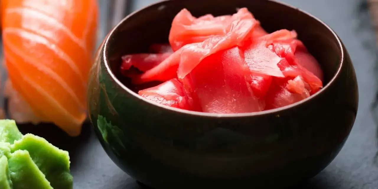 Miseczka z różowym imbirem do sushi, obok kawałek łososia i zielone wasabi.