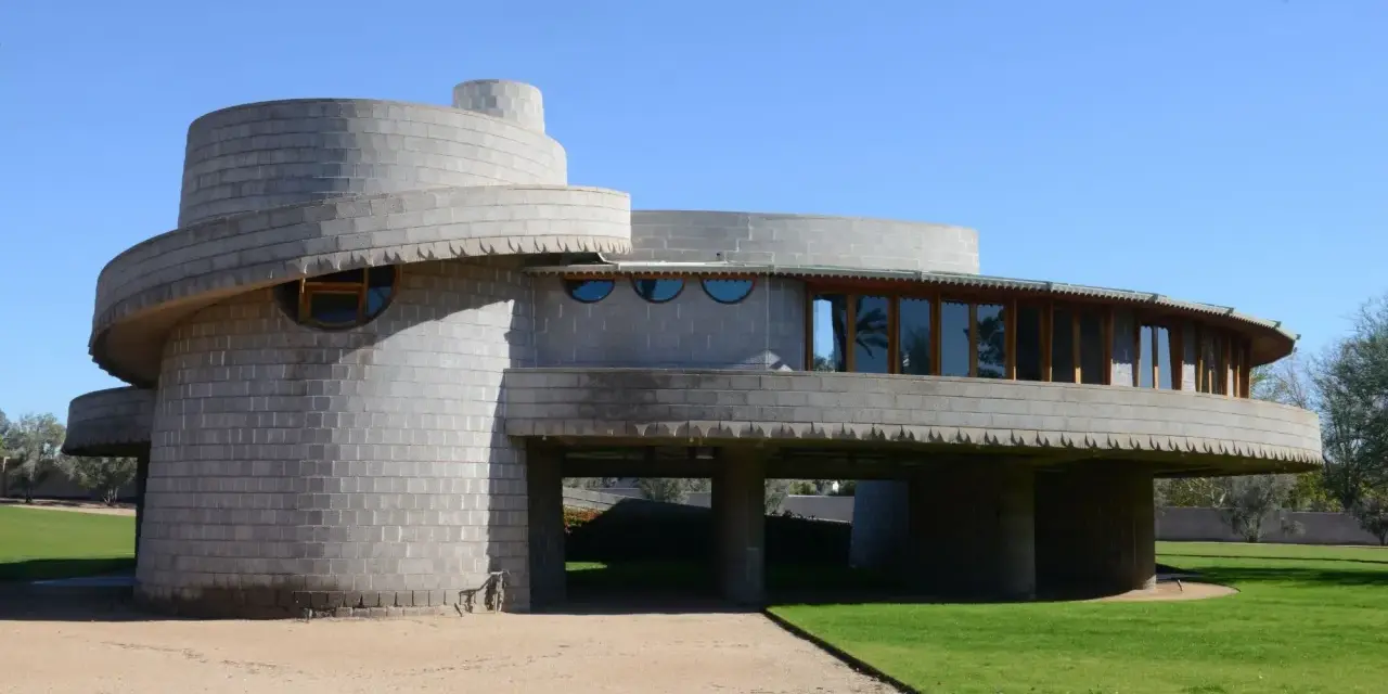 Bâtiment circulaire en béton, exemple des structures conçues par Frank Lloyd Wright, avec des fenêtres rondes et une façade en gradins.