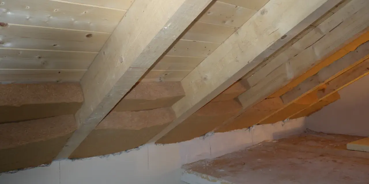 Isolamento tetto dall'interno fai da te: pannelli isolanti in fibra di legno tra le travi di legno grezzo, con sottotetto in perline.