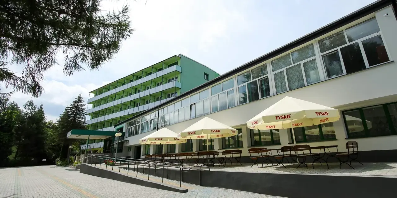 Tanie sanatorium prywatnie: zielony budynek z balkonami i tarasem z parasolami Tyskie.