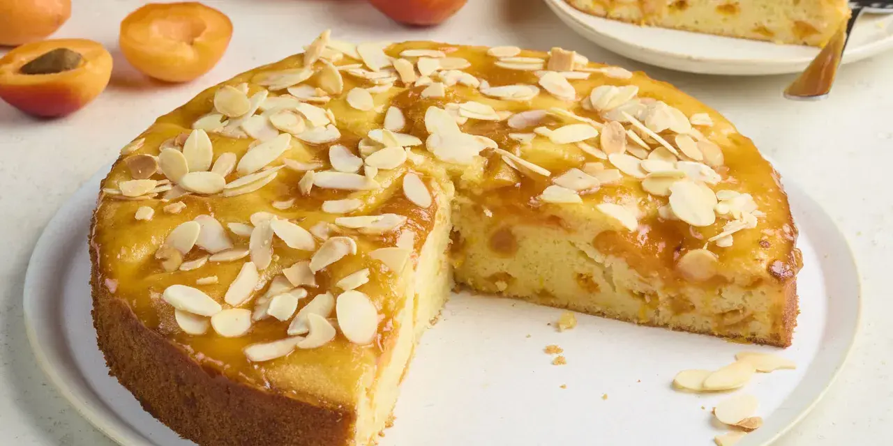 Saftiger aprikosenkuchen mit frischen aprikosen und Mandelblättchen, ein Stück bereits angeschnitten.