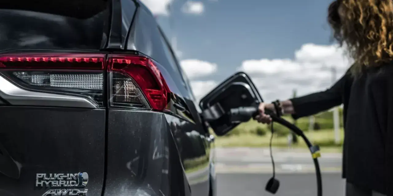 Kobieta podłącza ładowarkę do hybrydowego SUV-a. Zastanawiasz się, ile kosztuje ładowanie elektryka?