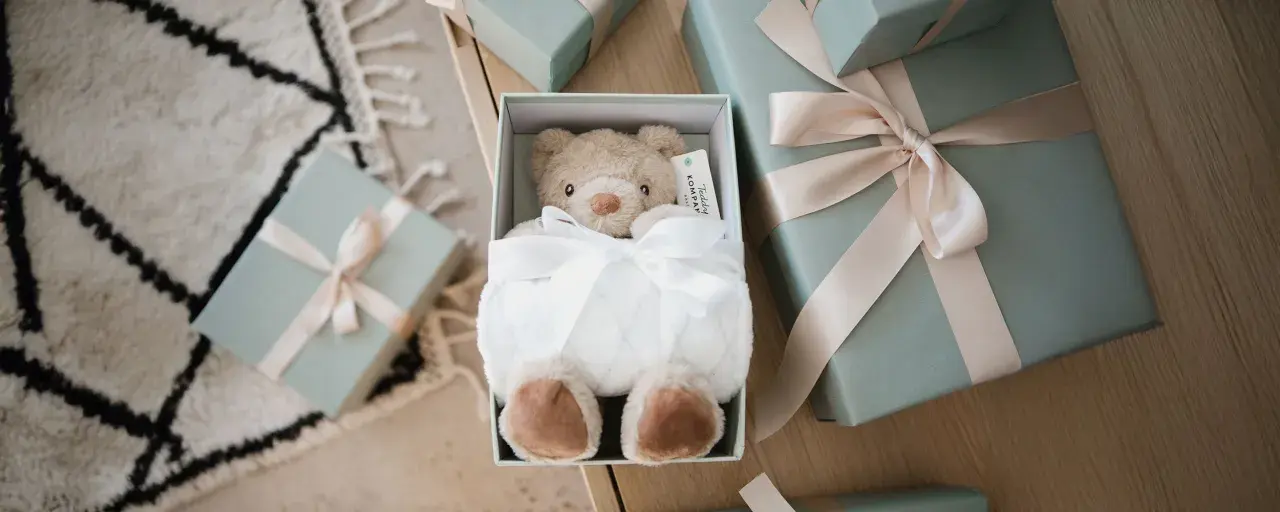 En mjuk nallebjörn i en presentbox, omgiven av fler presenter med ljusrosa band. En perfekt välkommen till världen present.