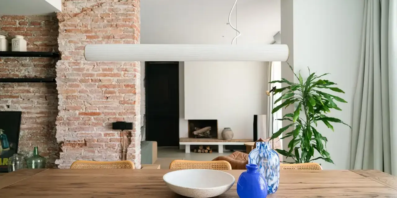 Salón con pared de ladrillo visto, mesa de madera con jarrones y planta.