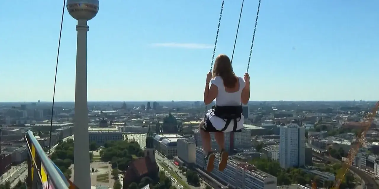 Frau schaukelt hoch über Alexanderplatz Berlin, mit Blick auf die Stadt und den Fernsehturm.