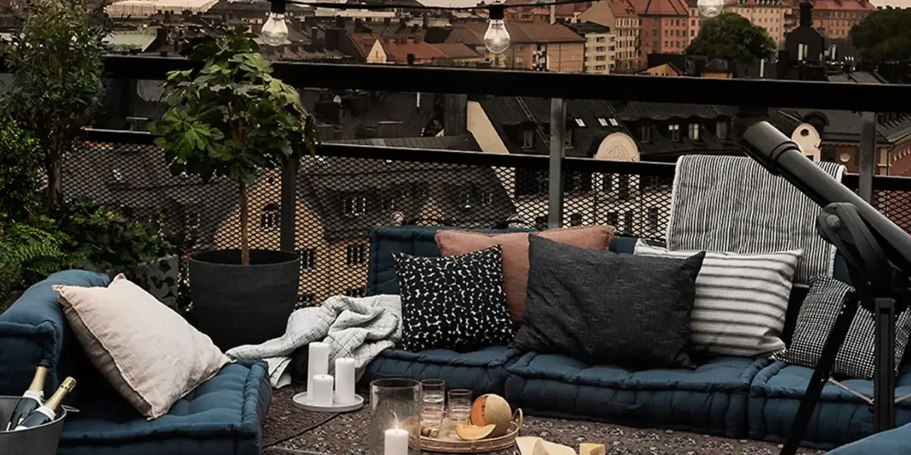Gemütliche Lounge-Ecke auf einem grossen Balkon mit Blick über die Stadt. Kissen, Decken, Kerzen und ein Teleskop laden zum Entspannen ein.