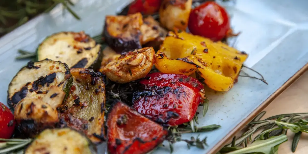 Gegrilltes Gemüse wie Zucchini, Paprika und Tomaten, garniert mit Rosmarin. Perfekt für Ihre nächsten BBQ Rezepte!