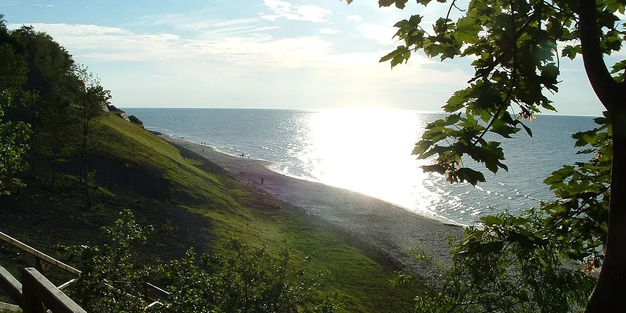 Słoneczny dzień nad morzem, łagodne zbocze porośnięte trawą schodzi do plaży. Jastrzębia Góra atrakcje to spacer po klifie i podziwianie widoków.