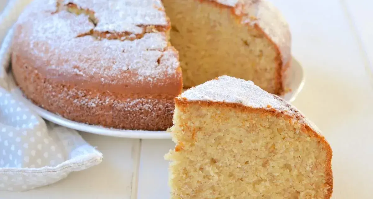 Una fetta di soffice torta di banane mature, spolverata di zucchero a velo, accanto alla torta intera su un piatto bianco.