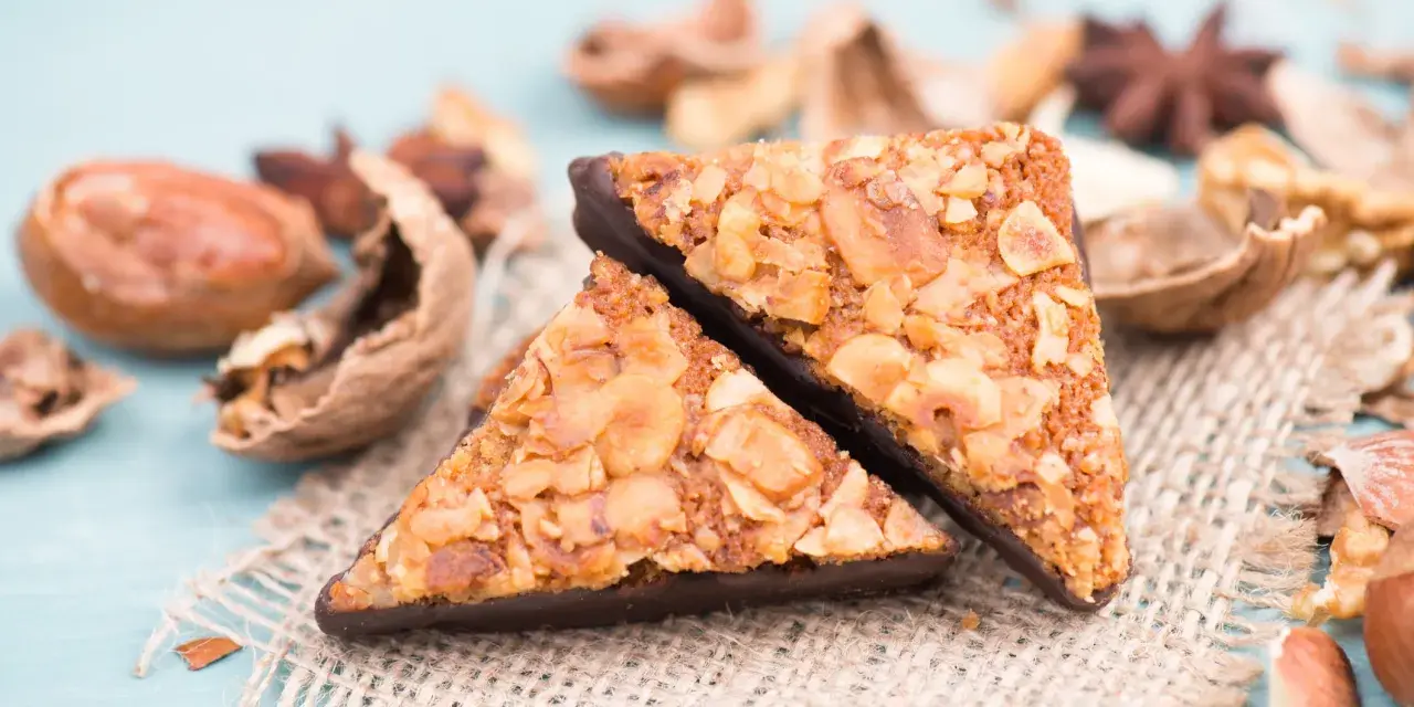 Zwei dreieckige Nussecken mit Schokoladenboden, bestreut mit gehackten Nüssen. Ein köstliches nussecken rezept zum Nachbacken.