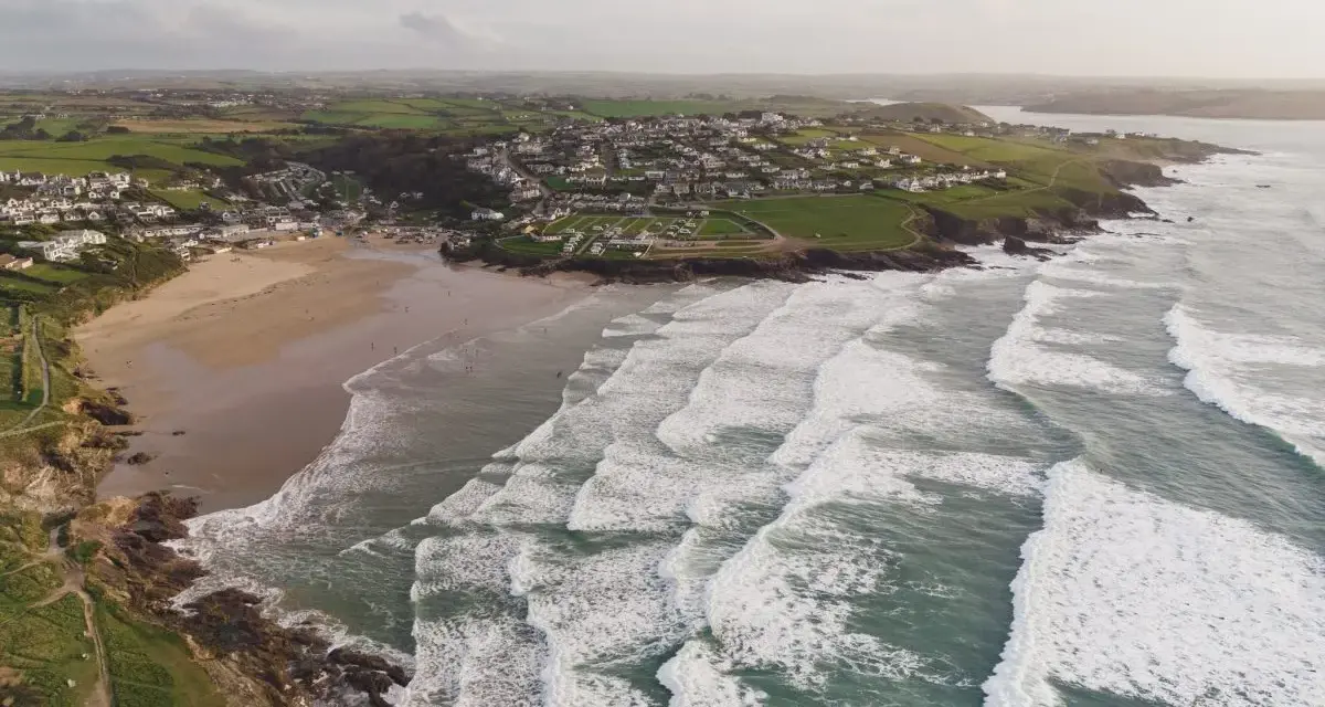 Aerial videography captures a coastal village with a sandy beach and rolling waves.