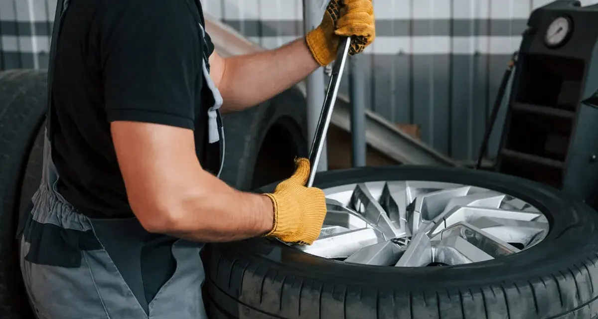 Mechanik w żółtych rękawicach używa klucza, by pokazać, jak zdjąć oponę z felgi.
