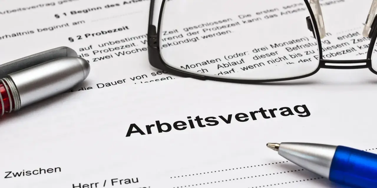 Ein Arbeitsvertrag mit Brille und Stiften liegt bereit. Die Probezeit ist ein wichtiger Teil des Arbeitsvertrags.