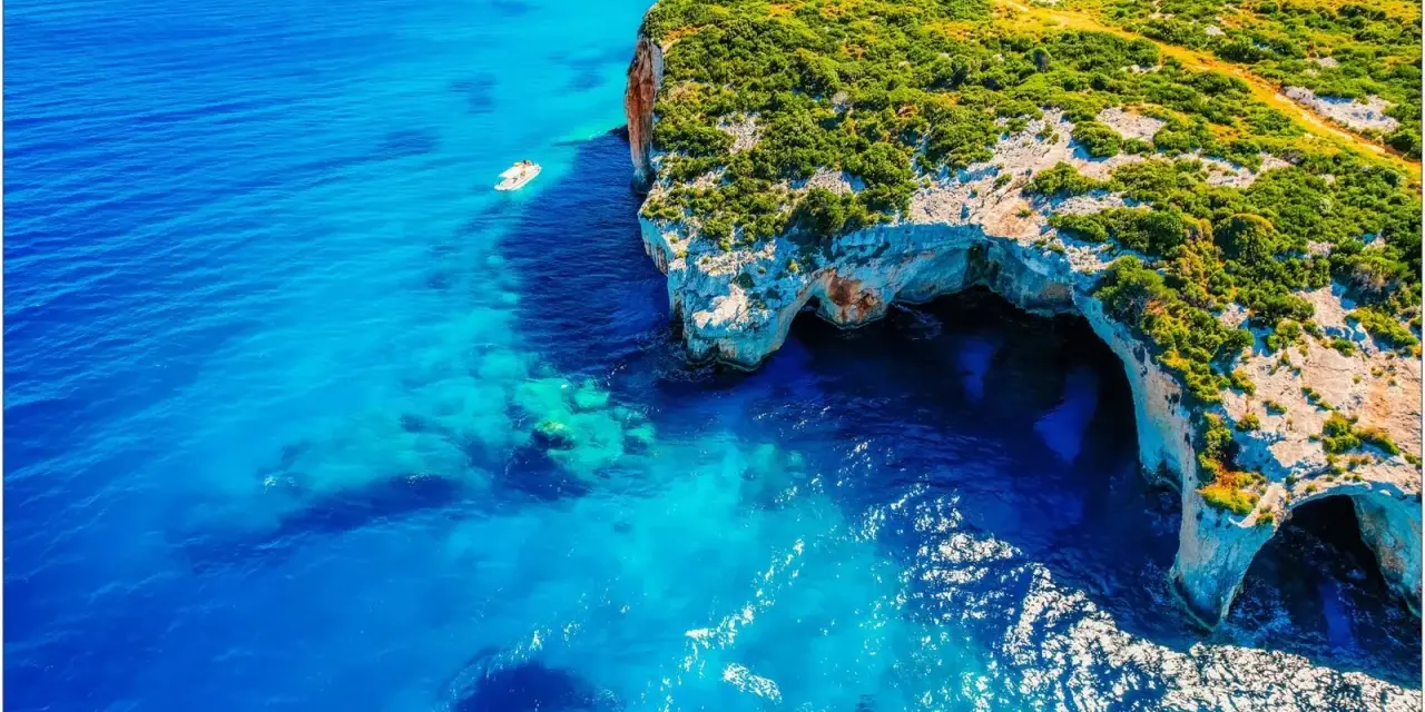 Błękitne morze i klify z jaskiniami to idealne miejsca na Zakynthos, co zobaczyć. Mała łódka kołysze się na falach.