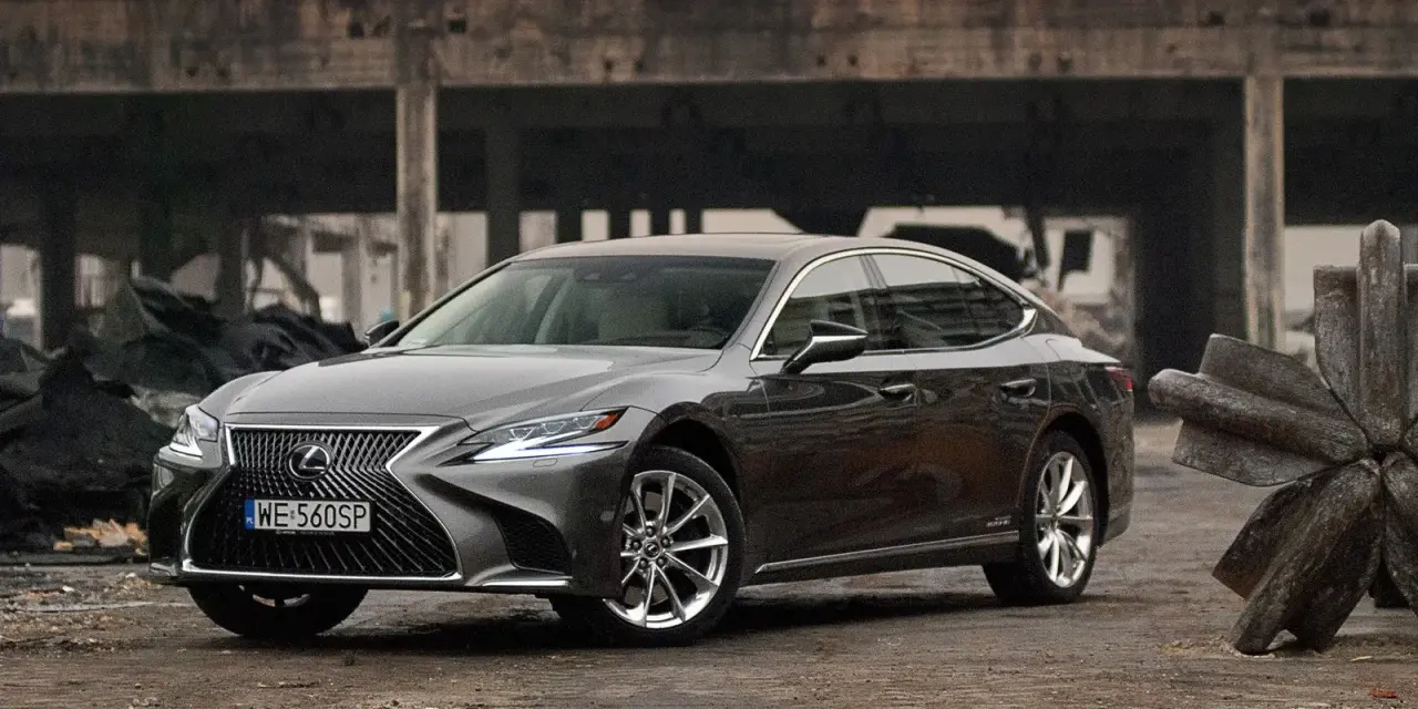 Szary Lexus LS 500h zaparkowany na tle zniszczonej budowli.