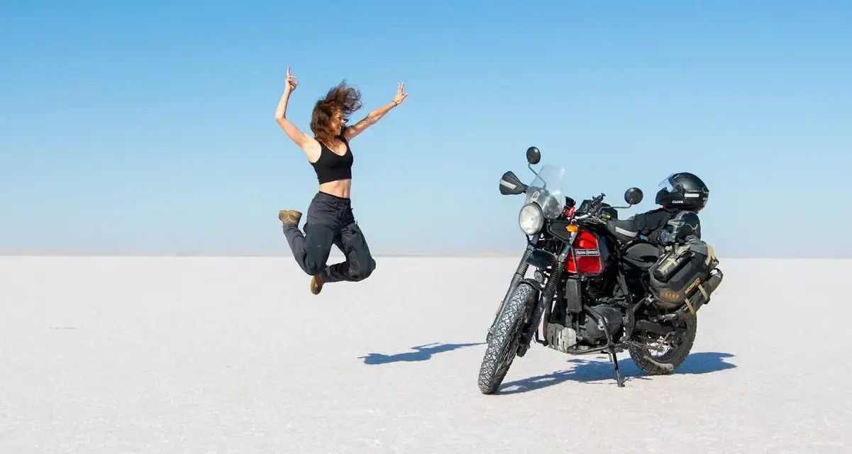 Donna salta di gioia su un deserto di sale, moto pronta per l'avventura. Questo è cosa significa on the road: libertà e scoperta.