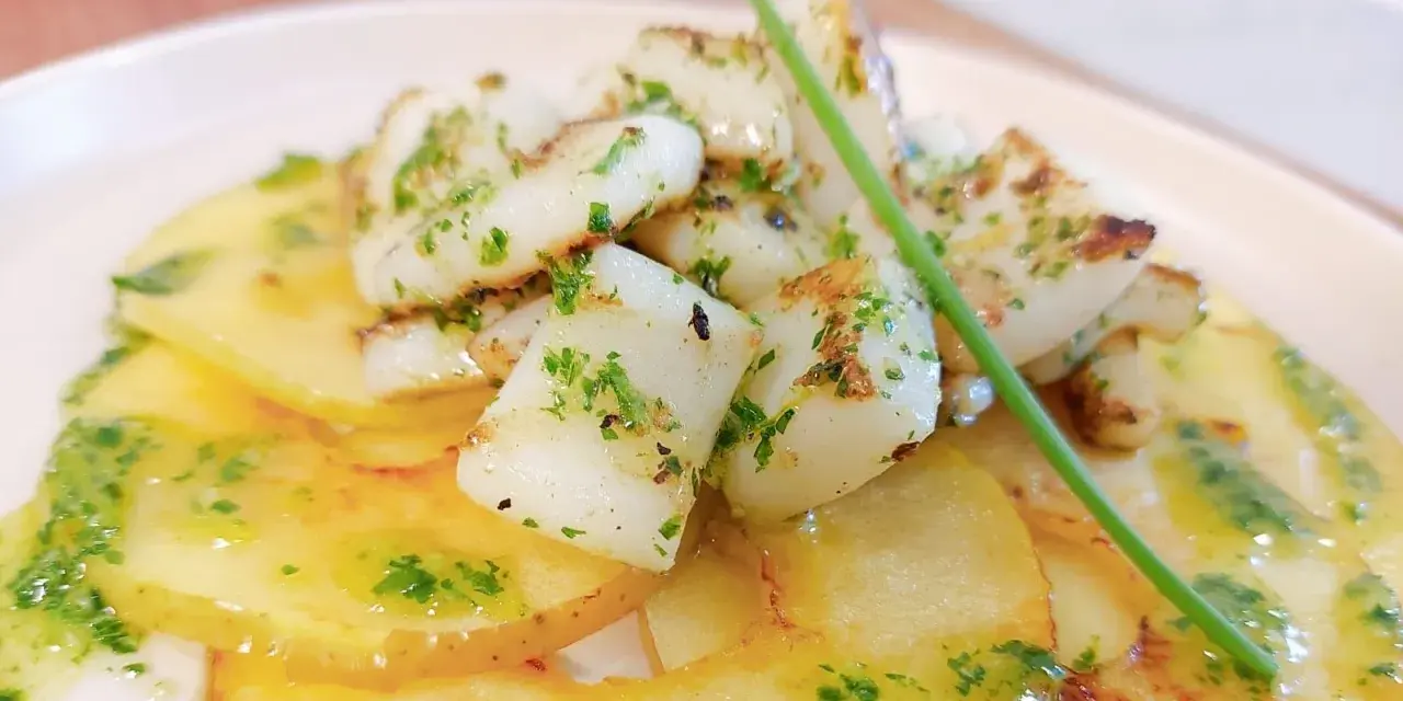 Delicioso plato de sepia al ajillo sobre patatas finas, con perejil picado y un toque de aceite de oliva.